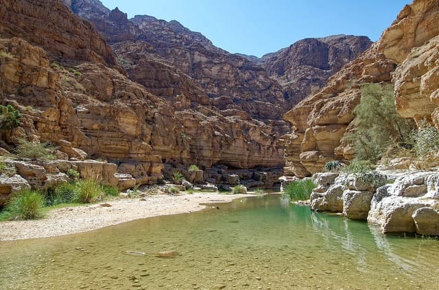 Paysage naturel d’un wadi à Oman, avec falaises rocheuses et eau turquoise, une étape incontournable lors d’un voyage à Oman - voyage sur mesure avec Nahra Travel, spécialiste Asie et Moyen-Orient.