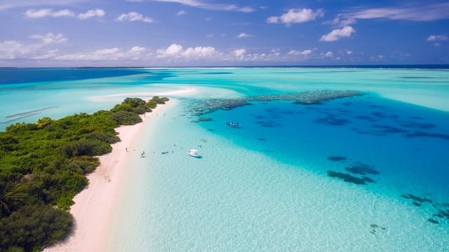 Plage paradisiaque aux Maldives avec sable blanc, eau turquoise et végétation luxuriante, une destination de rêve lors d’un voyage aux Maldives - voyage sur mesure avec Nahra Travel, spécialiste Asie et Moyen-Orient.
