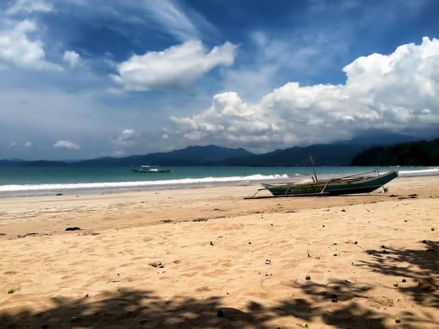Plage de sable doré aux Philippines avec une bangka traditionnelle et vue sur les montagnes, une expérience authentique lors d’un voyage aux Philippines - voyage sur mesure avec Nahra Travel, spécialiste Asie et Moyen-Orient.