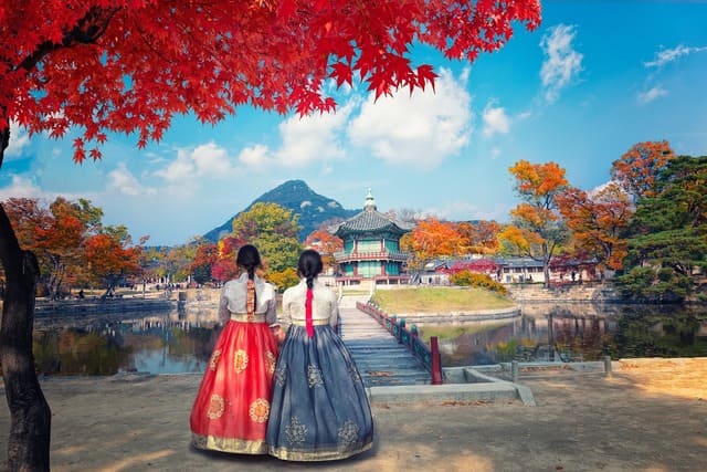 Deux femmes en hanbok traditionnel devant le palais Gyeongbokgung à Séoul, entouré de couleurs d’automne, une expérience culturelle unique lors d’un voyage en Corée du Sud - voyage sur mesure avec Nahra Travel, spécialiste Asie et Moyen-Orient.
