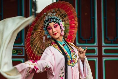 Nahra Travel organisation de voyage sur mesure travel planner Asie Europe Afrique Moyen-Orient - femme chinoise en costume traditionnel coloré, portant une coiffe ornée et tenant un éventail décoratif, dans un décor traditionnel chinois.